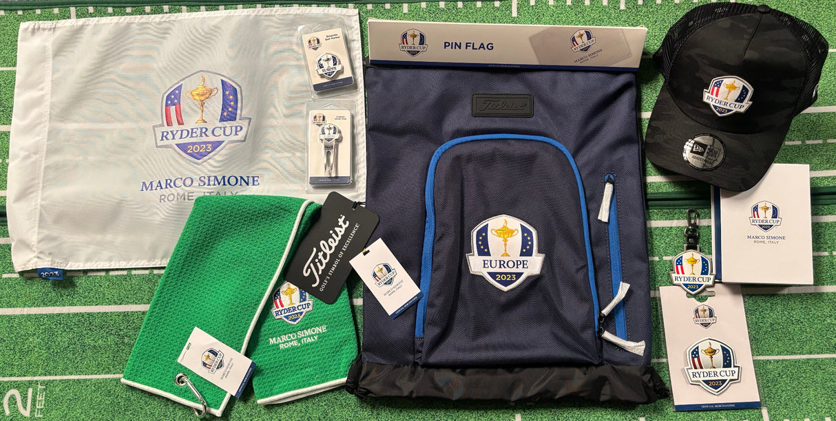 Ryder Cup merchandise including a bag, towel, hat, and other items on a grass surface.